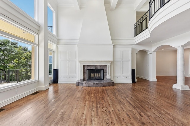 unfurnished living room with a towering ceiling, a fireplace, hardwood / wood-style flooring, beam ceiling, and decorative columns