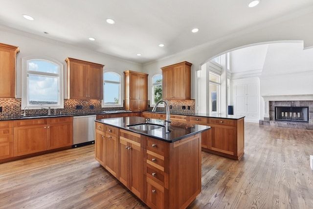 kitchen featuring stainless steel dishwasher, a tile fireplace, sink, and an island with sink