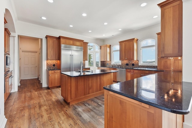 kitchen featuring sink, built in appliances, a center island with sink, and dark wood-type flooring