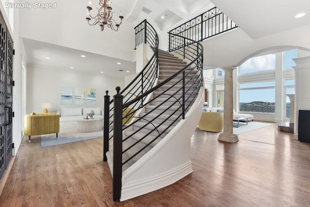 stairway with coffered ceiling, a towering ceiling, a notable chandelier, hardwood / wood-style flooring, and beam ceiling