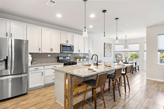 kitchen featuring pendant lighting, white cabinets, sink, an island with sink, and stainless steel appliances