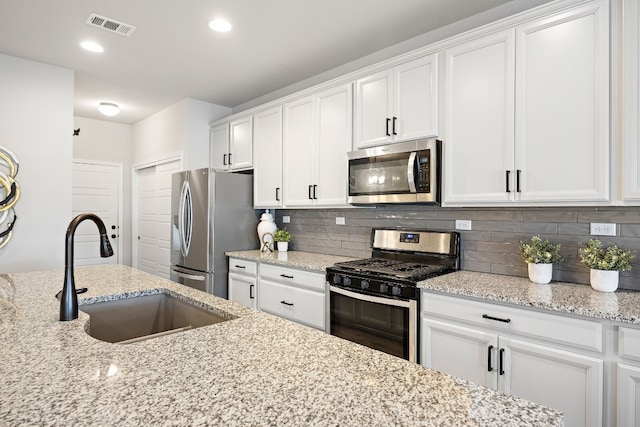 kitchen featuring appliances with stainless steel finishes, light stone counters, white cabinetry, and sink