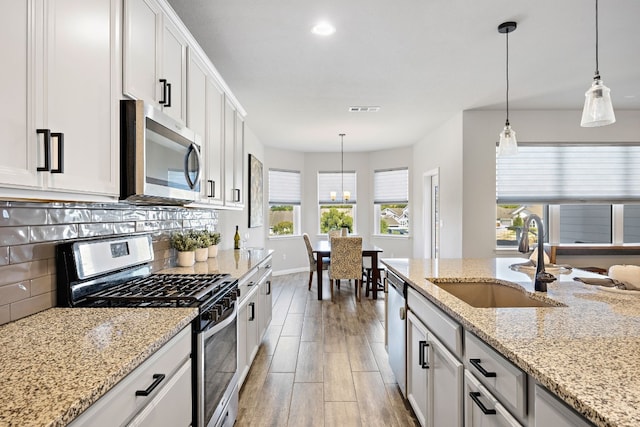 kitchen with hanging light fixtures, white cabinetry, sink, and stainless steel appliances