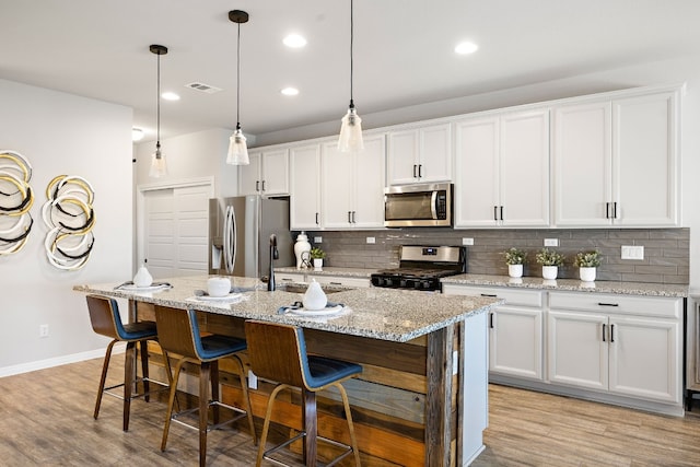 kitchen featuring white cabinetry, light hardwood / wood-style flooring, an island with sink, and appliances with stainless steel finishes