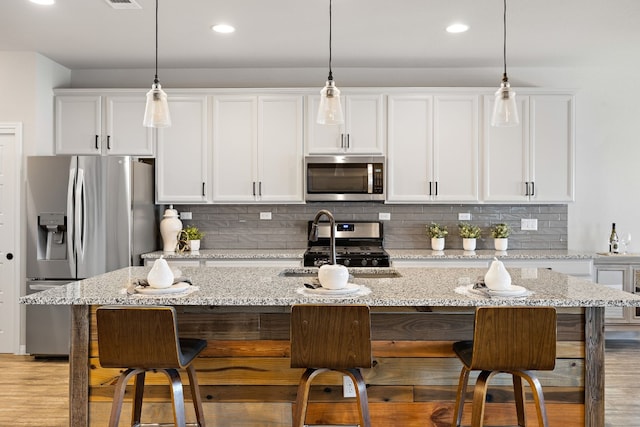 kitchen featuring white cabinets, light hardwood / wood-style flooring, an island with sink, light stone counters, and stainless steel appliances