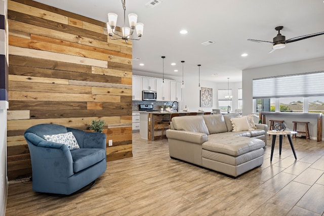 living room featuring wood walls, ceiling fan with notable chandelier, light hardwood / wood-style floors, and sink