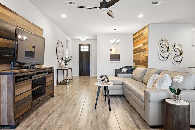 living room featuring ceiling fan with notable chandelier and light wood-type flooring