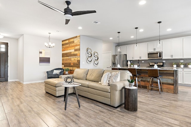 living room with ceiling fan with notable chandelier and light wood-type flooring