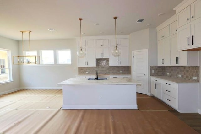 kitchen with white cabinetry, an island with sink, sink, and decorative light fixtures