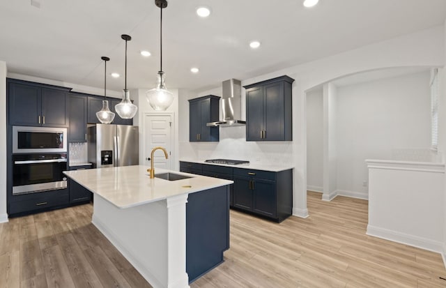 kitchen featuring wall chimney exhaust hood, stainless steel appliances, tasteful backsplash, sink, and a kitchen island with sink