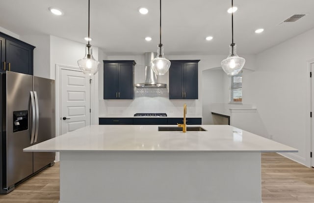 kitchen with pendant lighting, wall chimney range hood, stainless steel fridge, and a center island with sink