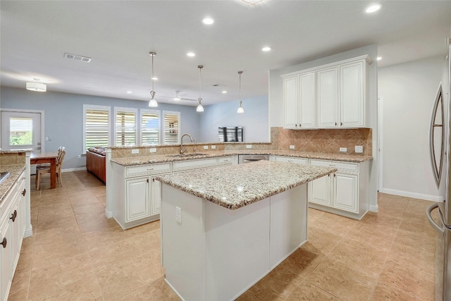 kitchen featuring sink, decorative light fixtures, kitchen peninsula, a kitchen island, and decorative backsplash