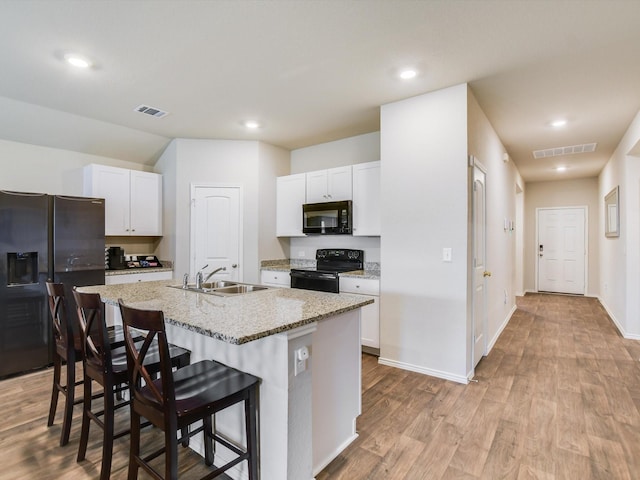 kitchen with white cabinets, black appliances, sink, a breakfast bar, and a center island with sink