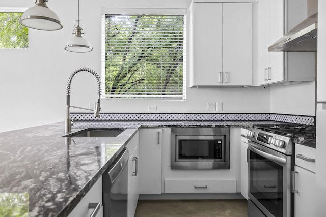 kitchen with white cabinets, wall chimney exhaust hood, stainless steel appliances, dark stone countertops, and sink