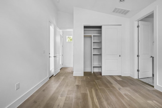 unfurnished bedroom featuring light hardwood / wood-style flooring, a closet, and vaulted ceiling