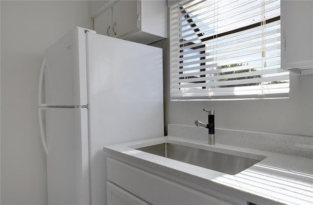 kitchen with white cabinetry, fridge, light stone counters, and sink