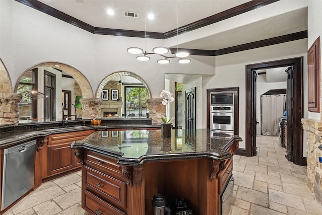 kitchen featuring appliances with stainless steel finishes, dark stone countertops, hanging light fixtures, ornamental molding, and a kitchen island