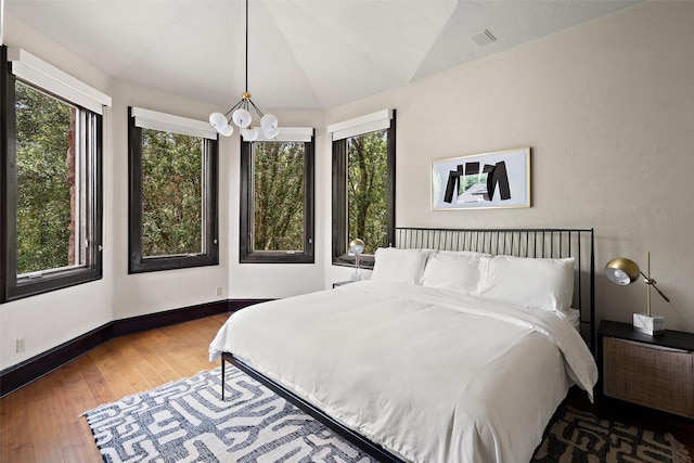 bedroom with hardwood / wood-style flooring, lofted ceiling, a chandelier, and multiple windows