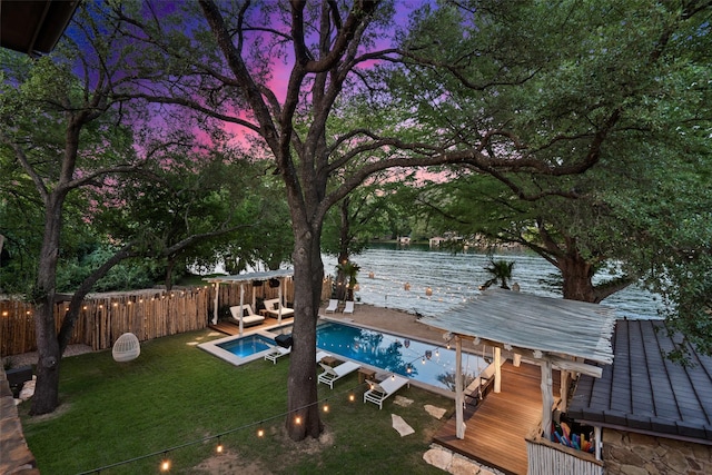 pool at dusk with a water view and a yard