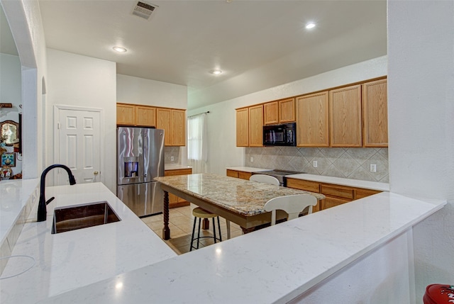 kitchen with decorative backsplash, stainless steel fridge, light stone countertops, and sink