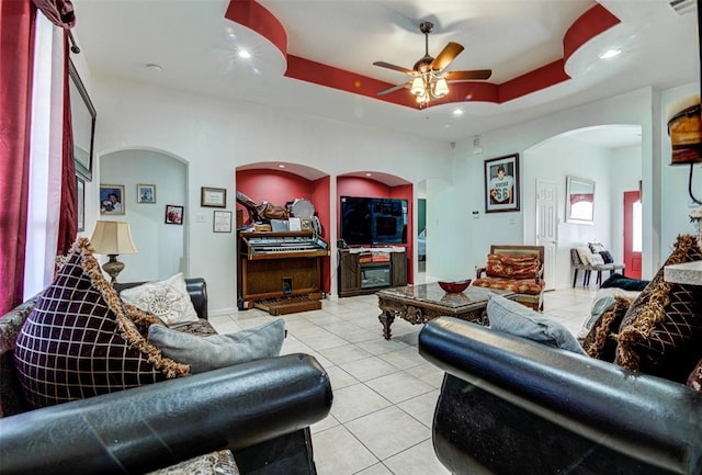 tiled living room with ceiling fan and a tray ceiling