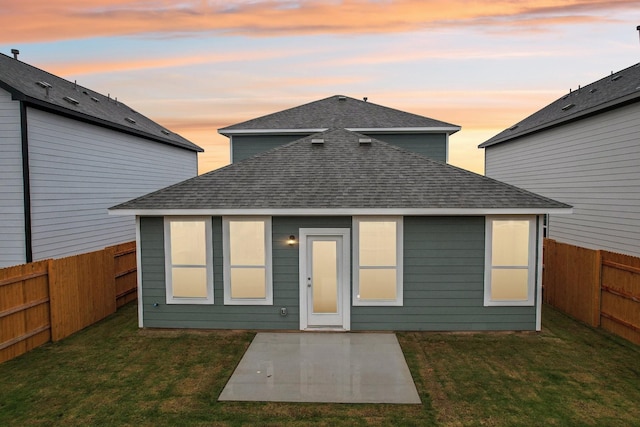 back house at dusk with a lawn and a patio