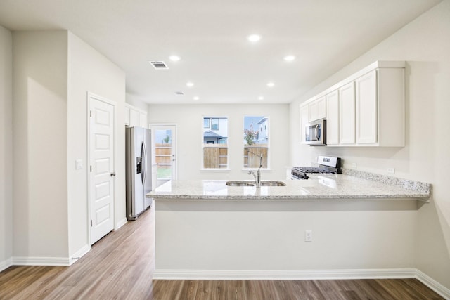 kitchen with sink, stainless steel appliances, light stone countertops, white cabinets, and kitchen peninsula