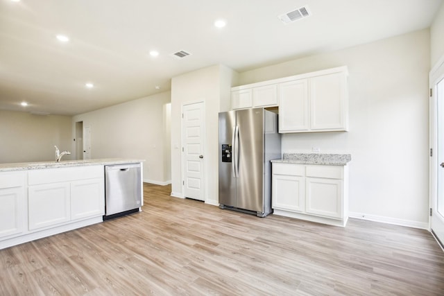 kitchen featuring light stone countertops, white cabinetry, appliances with stainless steel finishes, and light wood-type flooring