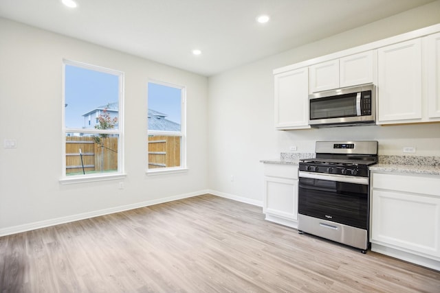 kitchen with light stone countertops, white cabinetry, appliances with stainless steel finishes, and light wood-type flooring