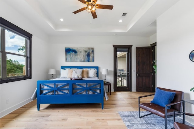 bedroom with a raised ceiling, baseboards, visible vents, and light wood finished floors