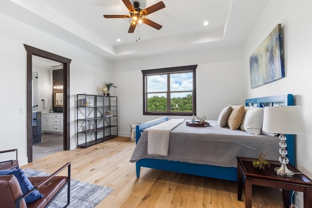 bedroom with recessed lighting, light wood-type flooring, a raised ceiling, and baseboards