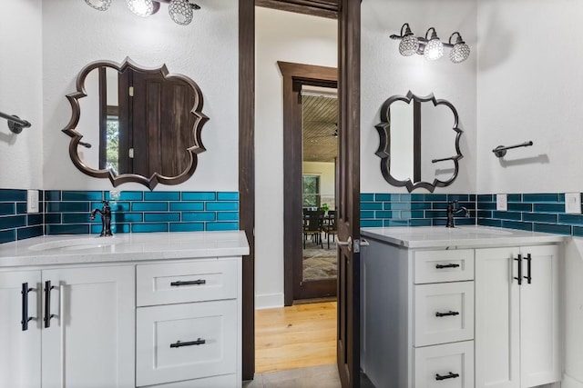 bathroom with two vanities, wood finished floors, tasteful backsplash, and a sink