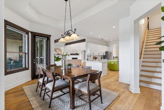 dining room with light wood-style flooring, a tray ceiling, recessed lighting, stairway, and baseboards