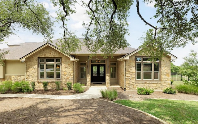 craftsman-style home with french doors, stone siding, roof with shingles, and fence