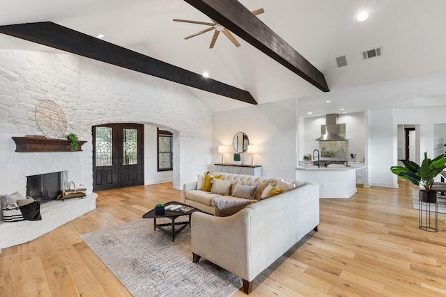 living area featuring visible vents, beamed ceiling, high vaulted ceiling, light wood-style flooring, and arched walkways