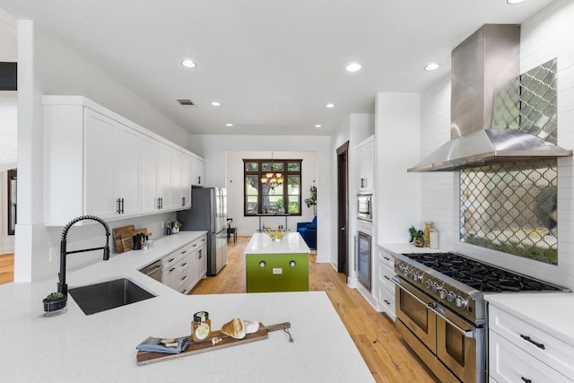 kitchen with visible vents, a sink, light countertops, appliances with stainless steel finishes, and wall chimney range hood