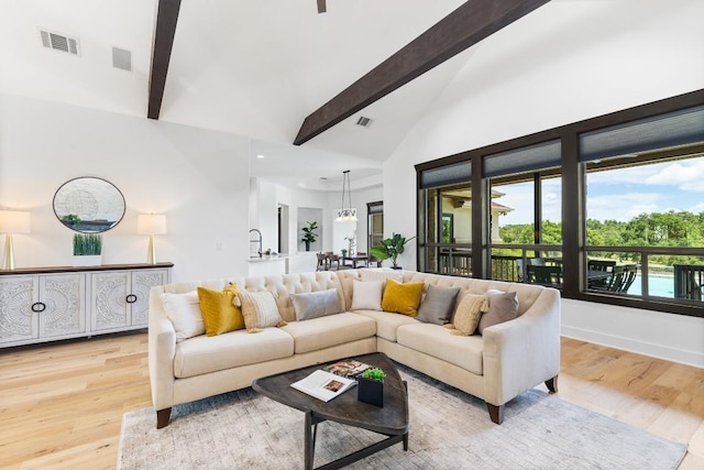 living area with visible vents, beamed ceiling, and light wood finished floors