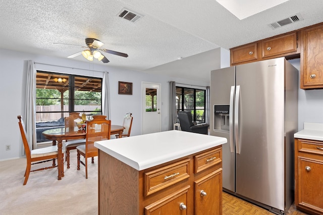 kitchen with stainless steel fridge with ice dispenser, ceiling fan, a center island, and a textured ceiling