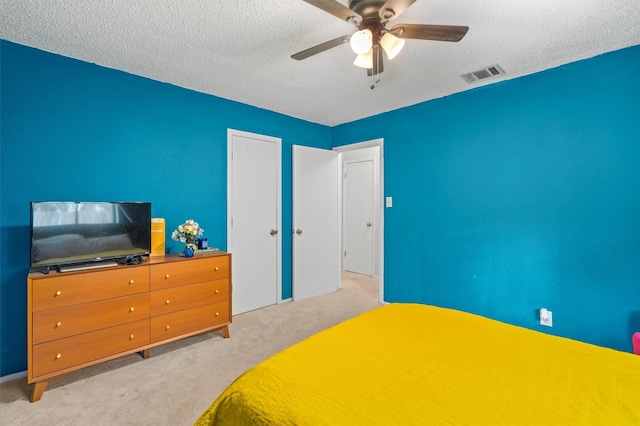 bedroom with ceiling fan, light colored carpet, and a textured ceiling