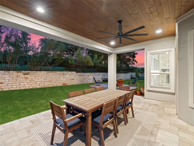 patio terrace at dusk with a yard, outdoor dining area, a fenced backyard, and a ceiling fan