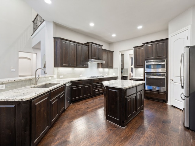 kitchen with a center island, stainless steel appliances, backsplash, dark wood-type flooring, and a sink