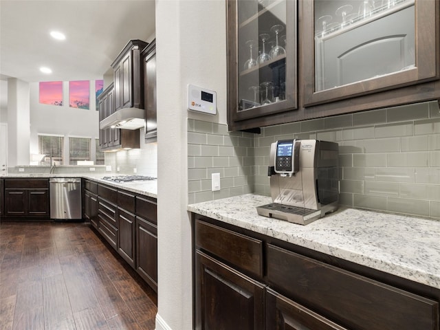 kitchen featuring light stone counters, dark wood finished floors, appliances with stainless steel finishes, glass insert cabinets, and dark brown cabinetry