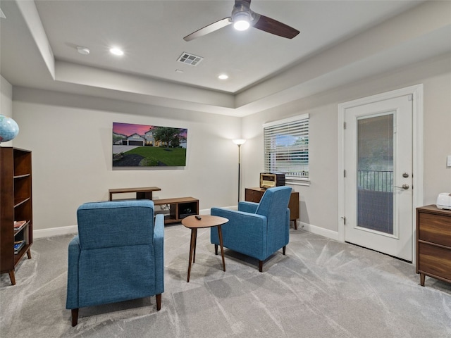 living area with visible vents, baseboards, a raised ceiling, and light colored carpet