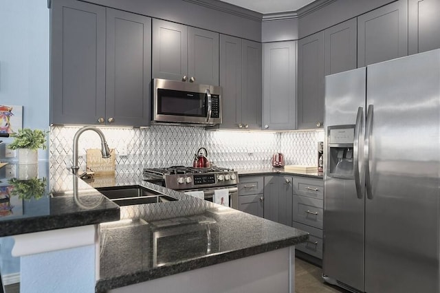 kitchen with stainless steel appliances, kitchen peninsula, backsplash, gray cabinets, and dark stone countertops