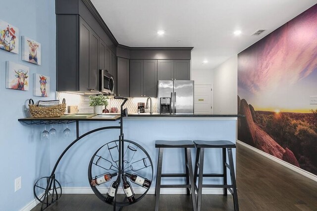 kitchen with decorative backsplash, appliances with stainless steel finishes, kitchen peninsula, and dark hardwood / wood-style flooring