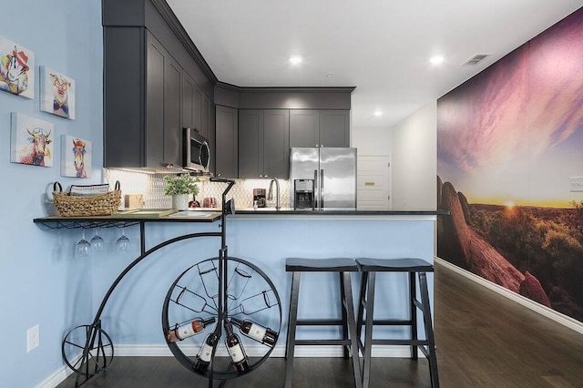 kitchen with appliances with stainless steel finishes, dark wood-type flooring, backsplash, and kitchen peninsula