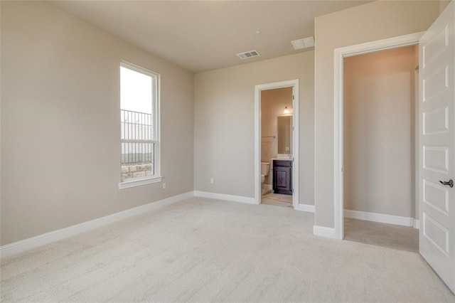 unfurnished bedroom featuring light carpet, multiple windows, and ensuite bathroom