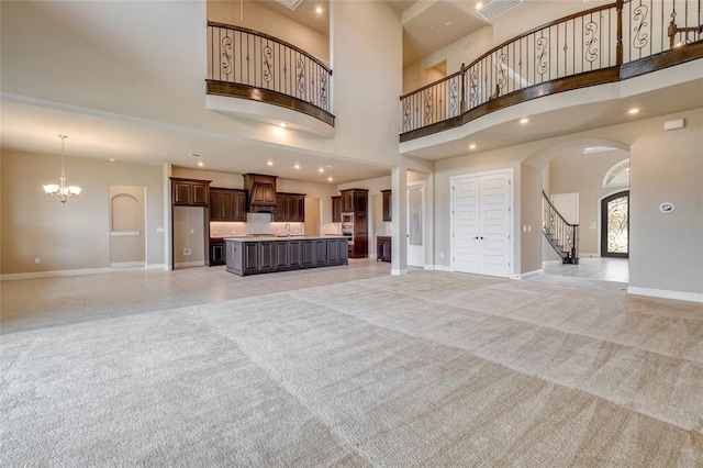 unfurnished living room featuring sink, an inviting chandelier, light colored carpet, and a high ceiling