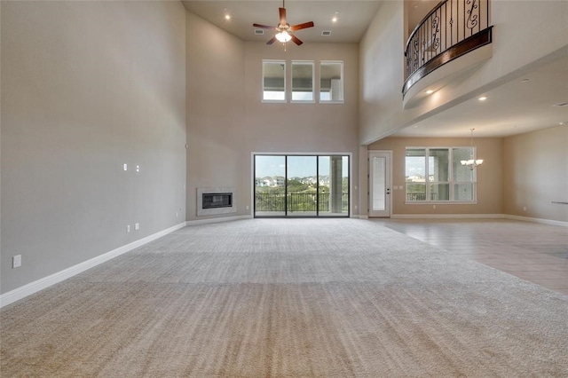 unfurnished living room featuring a high ceiling, light carpet, and ceiling fan with notable chandelier