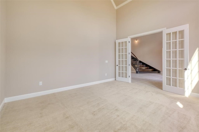 carpeted spare room with high vaulted ceiling and french doors